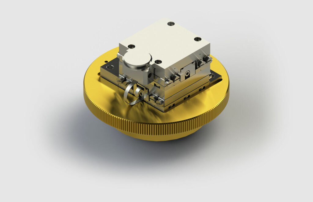 Eine Nahaufnahme eines metallischen mechanischen Tische-Bauteils mit goldener Basis und silberner Mechanik auf der Oberseite, mit verschiedenen Schrauben und Teilen. Das Bauteil ist vor einem neutralen, hellgrauen Hintergrund platziert.